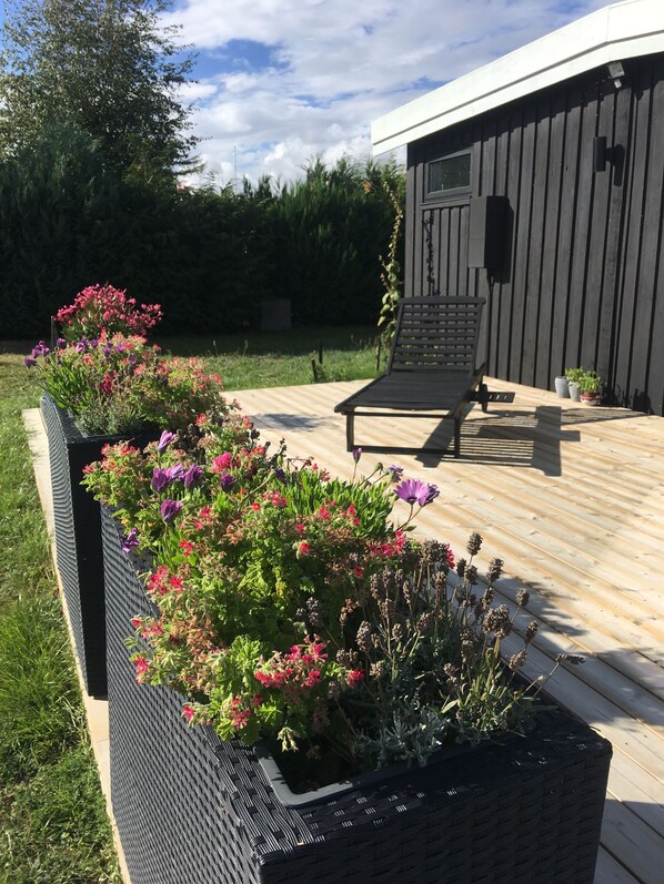 Un terrazzo in legno con mobili da esterno, una fioriera con fiori e un edificio sullo sfondo.