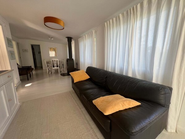 A living room with a black leather sofa, two yellow cushions, a dining area with a table and chairs, and a fireplace.