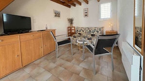 A cozy room with a TV on a wooden cabinet, a patterned sofa, a small table with a lamp, and a radiator. - Charming house near the beach - 4 guests (Saint-Georges-d'Oléron)