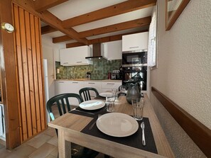 Ein Essbereich mit einem Holztisch, gedeckt für zwei Personen, einer Küche im Hintergrund und einer Holzboden.