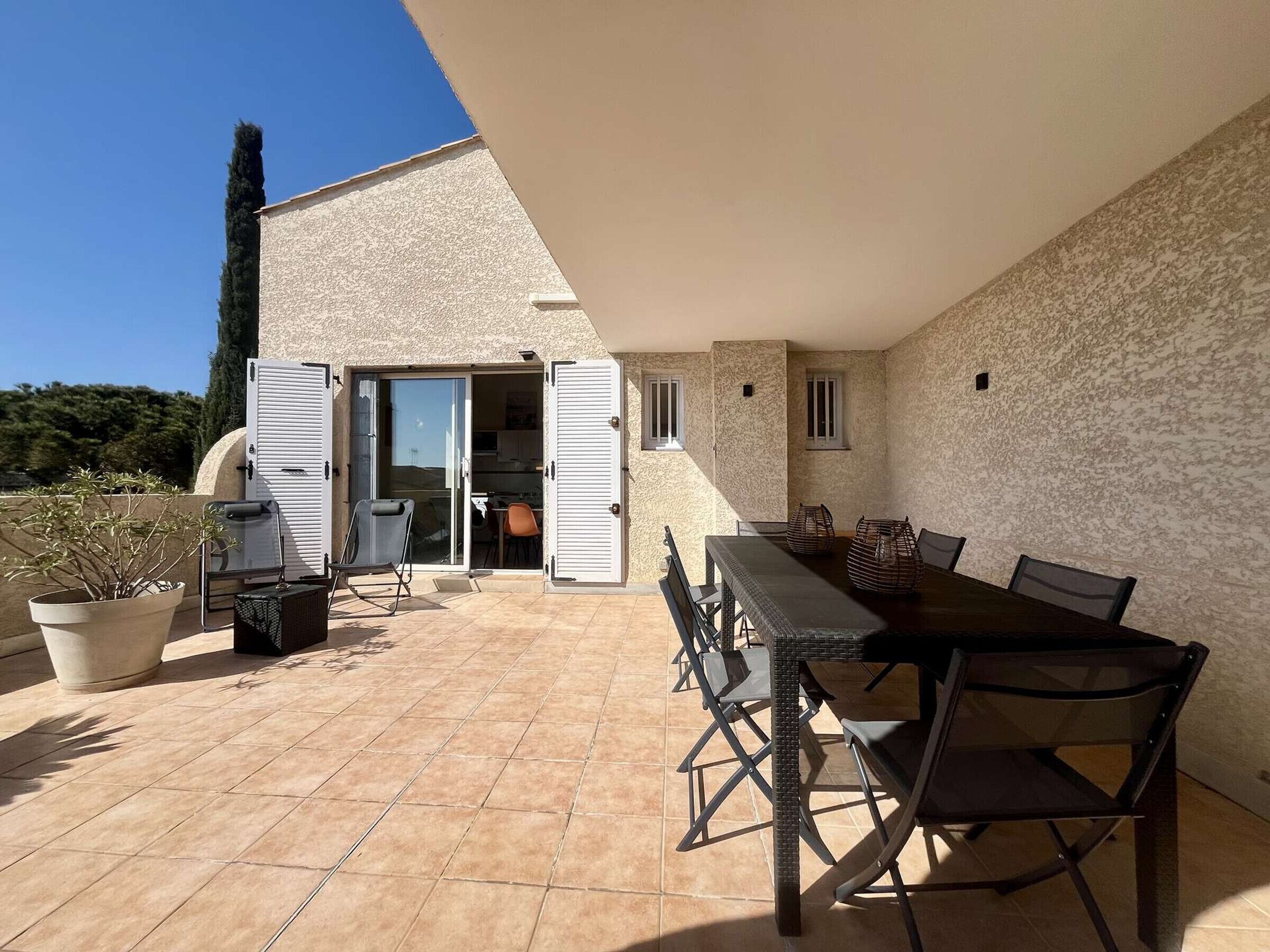 Une terrasse extérieure avec une table à manger, des chaises et un pot de fleurs.