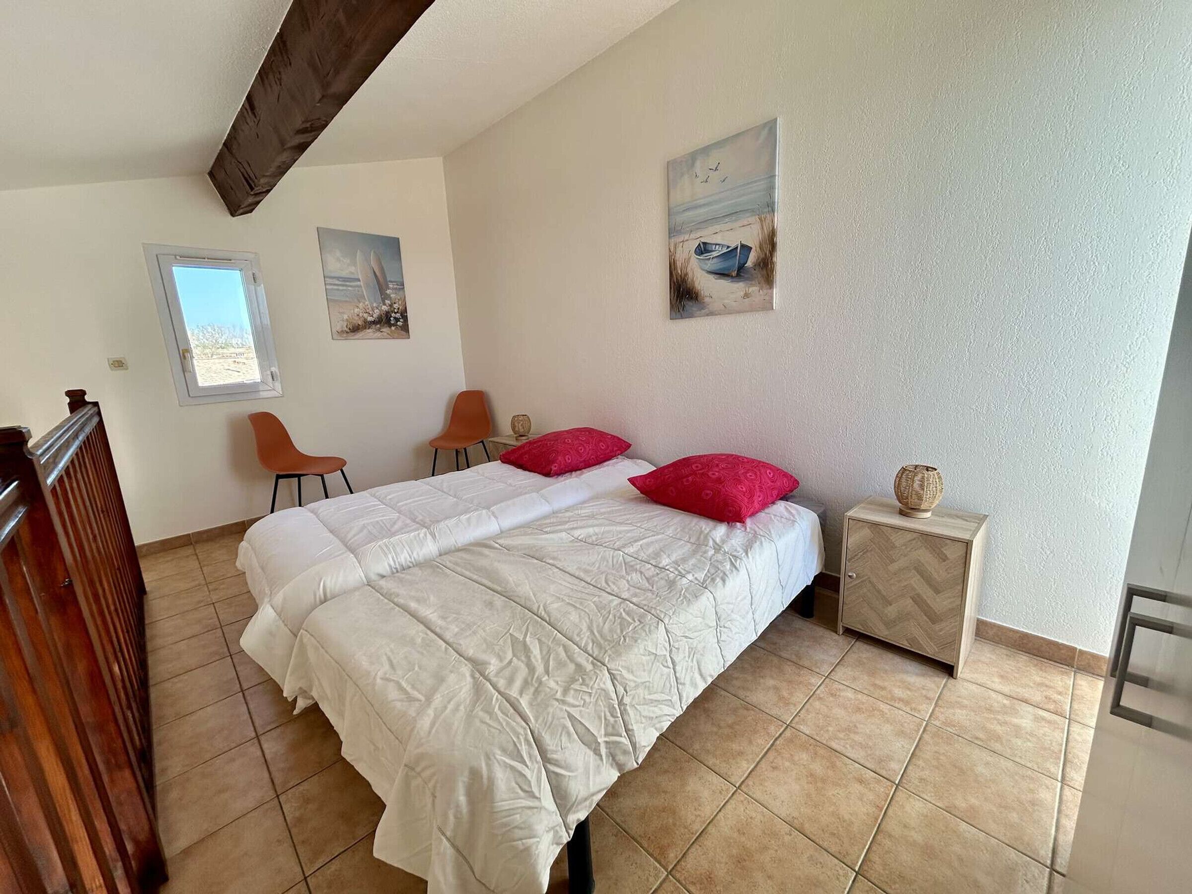 A bedroom with a bed, two chairs, a small table, and artwork on the walls.