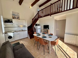 A compact kitchen with a washing machine, a dining area with a table set for four, and a staircase leading to an upper level. - Bright apartment near the beach - 4 guests (Cap d'Agde)