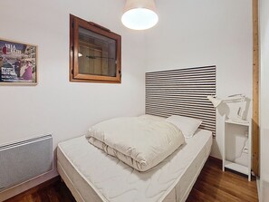 Ein Schlafzimmer mit einem Bett, einem Fenster mit Jalousien, einem Heizkörper, einem Schreibtisch mit Lampe und einem Poster an der Wand.