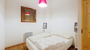 A bedroom with a bed, a window with a red light, a radiator, and a wooden door. - Spacious duplex near Super Châtel (Châtel)