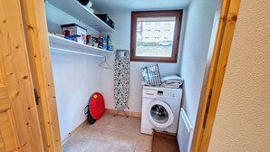 A laundry room with a washing machine, a drying rack, a red chair, and a window. - Spacious duplex near Super Châtel (Châtel)