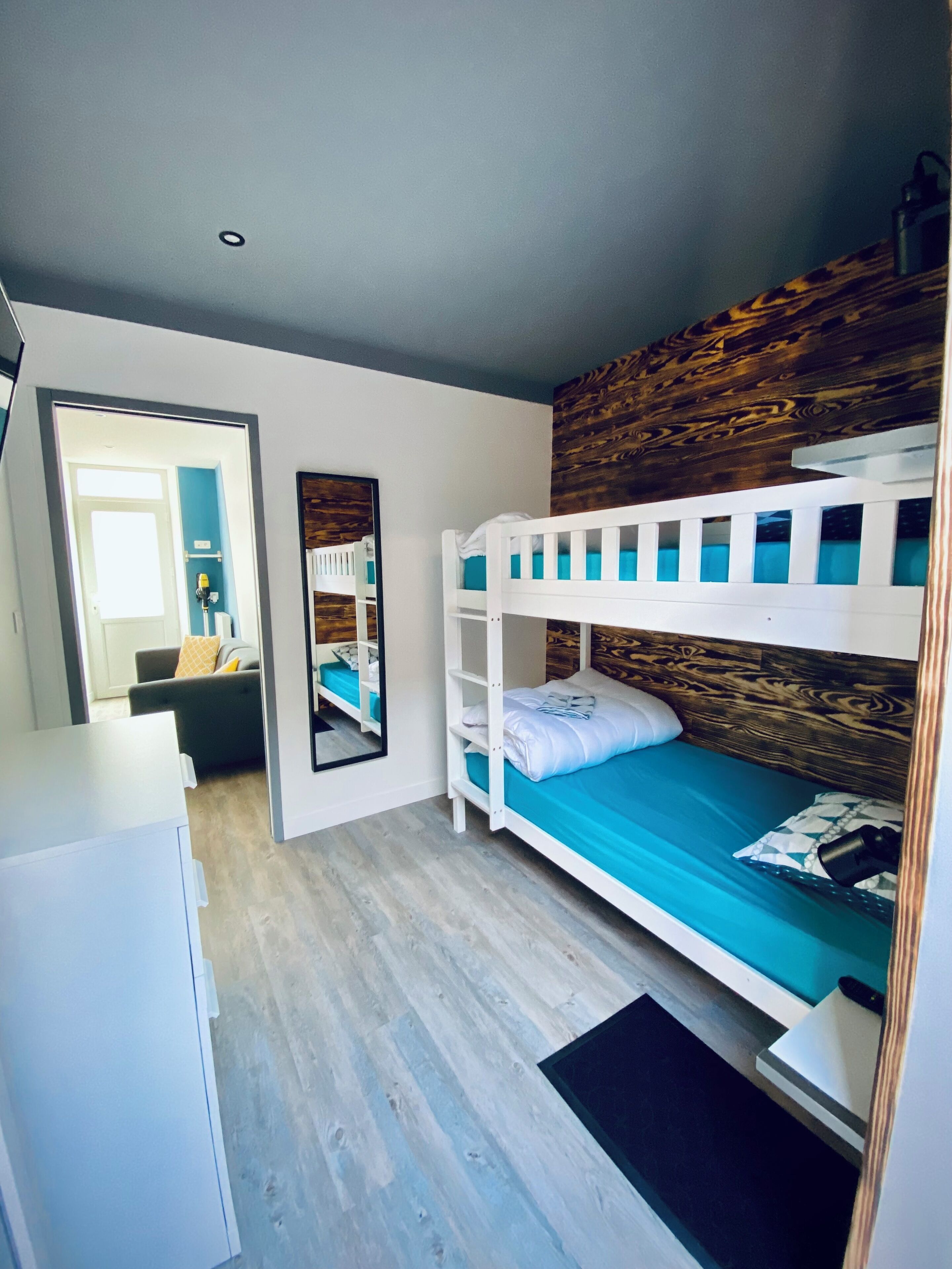 Un lit superposé avec une tête de lit en bois, un miroir, un bureau et une chaise, dans une pièce dont le sol est de couleur claire.