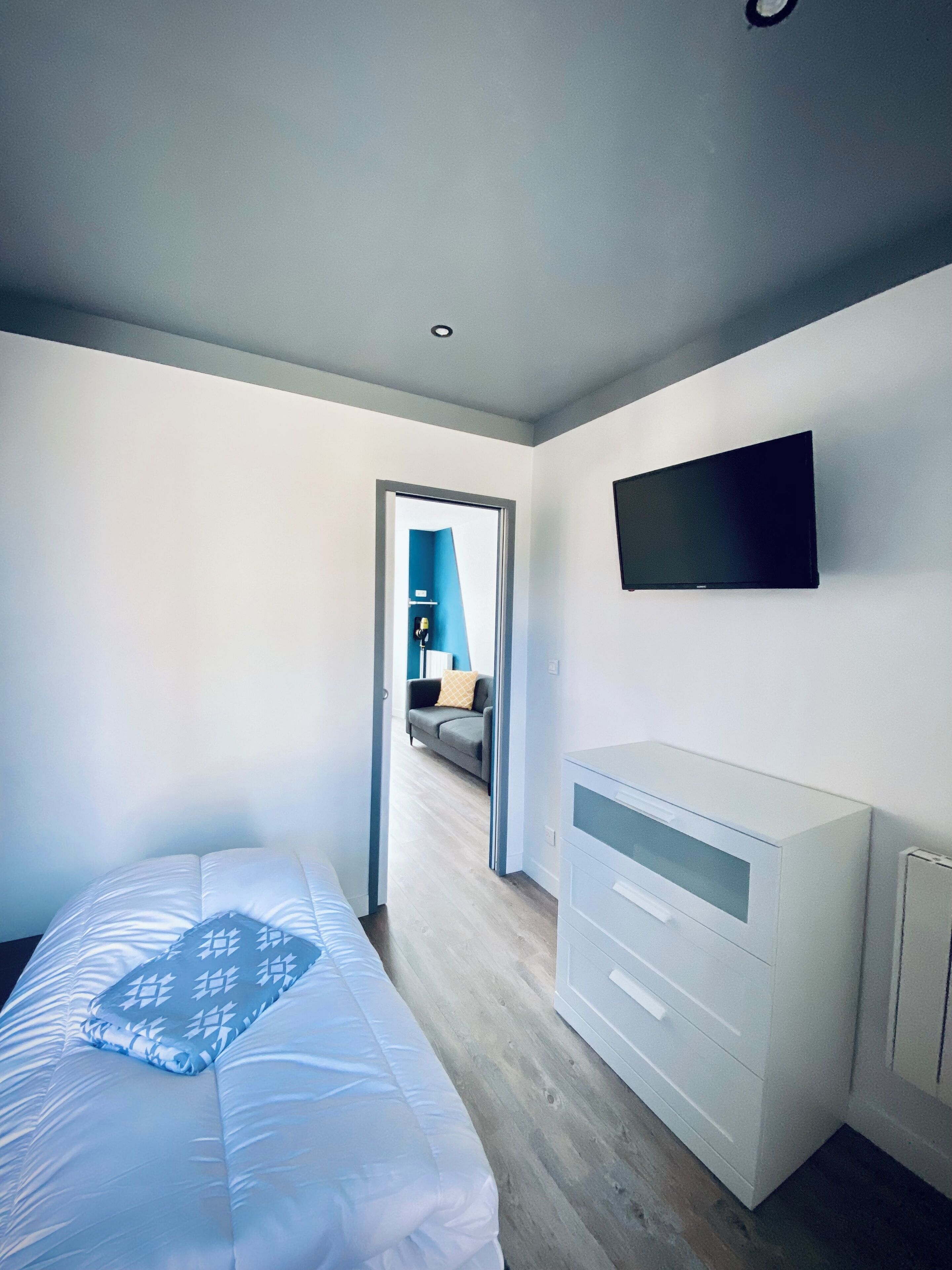 A bedroom with a bed, a dresser, and a TV mounted on the wall.