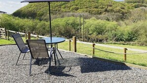 Un área de estar al aire libre con una mesa y sillas, una sombrilla y vistas a una colina.