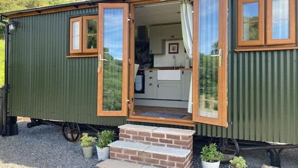 Una casa móvil con área de cocina, un pequeño porche con escalones y plantas en macetas.