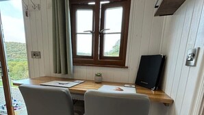 Una habitación con una mesa de madera, dos sillas grises, una ventana con cortinas y un radiador.