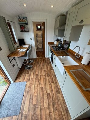 A compact kitchen with wooden flooring, a dining area, and white cabinetry.