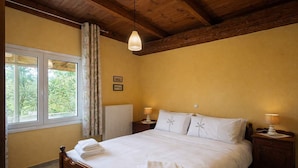 Quarto com cama de madeira, duas mesas de cabeceira com abajures, uma janela com cortinas e um radiador.