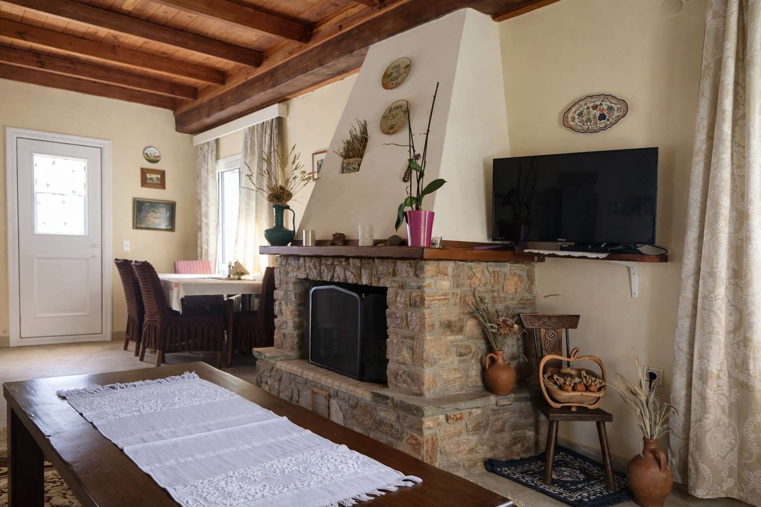 A cozy living room with a stone fireplace, a flat-screen TV, and a dining area with chairs and a table.