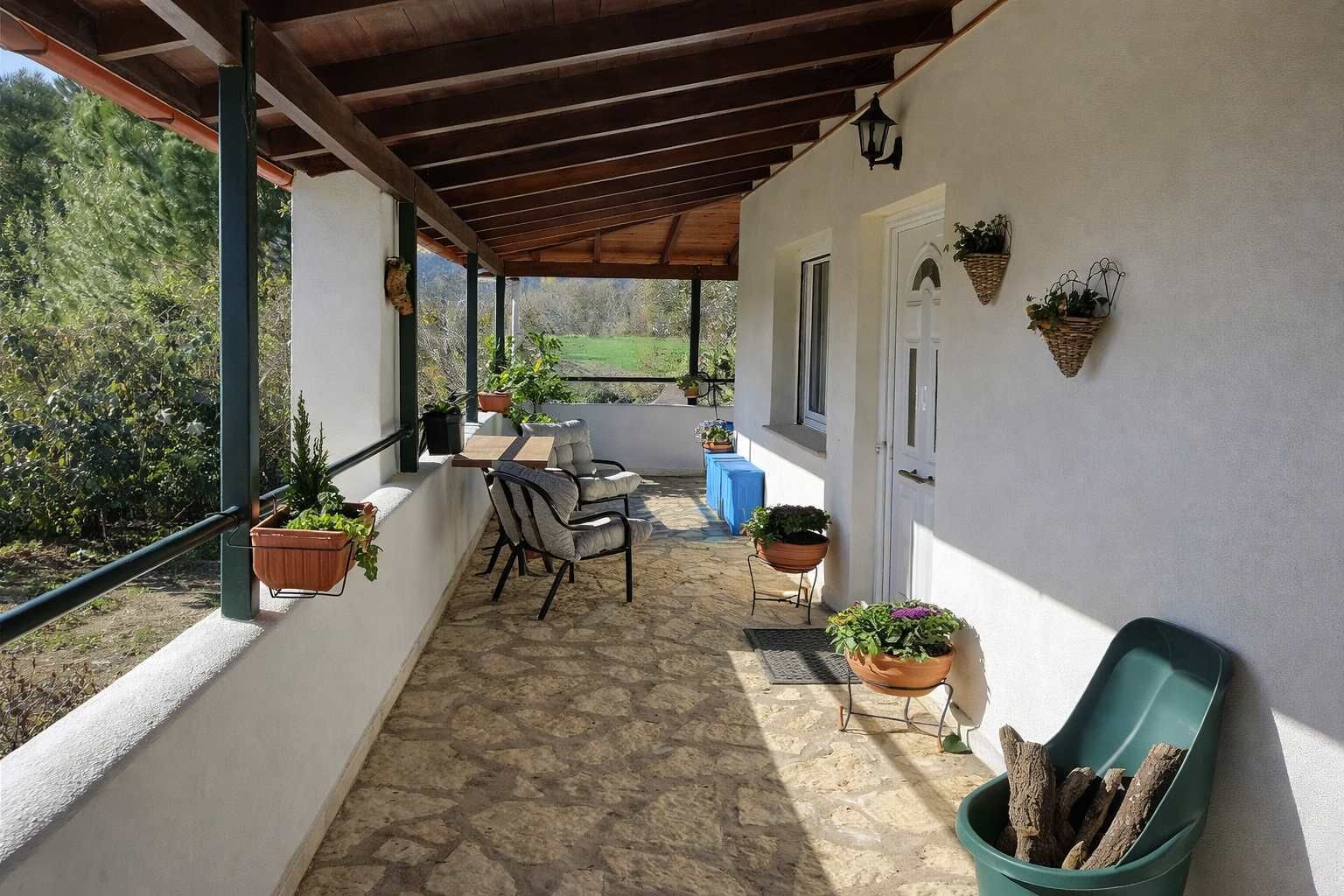 Un patio techado con mesa y sillas, plantas en macetas y vistas al follaje.