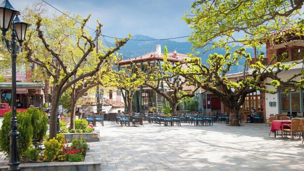 A courtyard with outdoor seating, trees, and buildings in the background. - Villa Dorothy - Mountain View Retreat Polydrosos (Delphi)