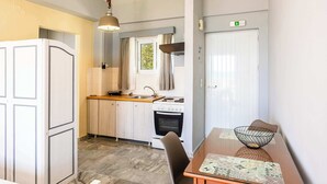 A compact kitchen with a refrigerator, stove, sink, and a dining table with a bowl. - Beachfront Nest Memi Koroni-seaheaven House B1 (Pylos-Nestoras)