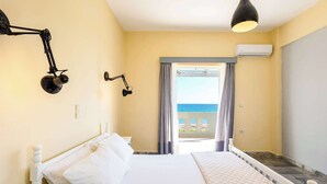 A bedroom with a bed, two wall-mounted lamps, an air conditioning unit, and a view of the sea through a window. - Beachfront Nest Memi Koroni-seaheaven House B1 (Pylos-Nestoras)