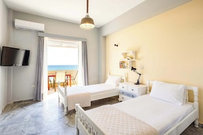 Een hotelkamer met twee bedden, een televisie, een boekenkast en uitzicht op zee.
