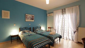 A bedroom with two beds, a nightstand, a chair, a radiator, and a window with curtains.