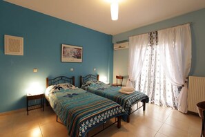 Quarto com duas camas, uma mesa de cabeceira, uma cadeira, um radiador e uma janela com cortinas.