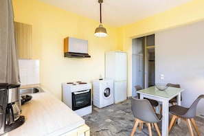 A compact kitchen with a stove, washing machine, and a dining area with a table and chairs. - Beachfront Nest Memi Koroni-seaheaven House A1 (Pylos-Nestoras)