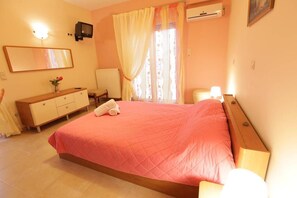 A bedroom with a bed, a dresser, a mirror, a television, and a window with curtains. - Bussiness Maisonette Getaway 5 min From the Beach (Kymi-Aliveri)