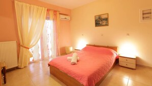 A bedroom with a bed, a nightstand, a chair, a radiator, and a window with curtains. - Bussiness Maisonette Getaway 5 min From the Beach (Kymi-Aliveri)