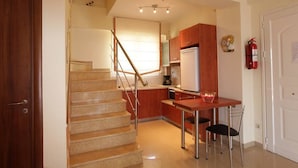 Een keuken met een houten trap, een witte koelkast en een kleine eettafel met twee stoelen.