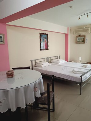 A room with two beds, a round table with a floral tablecloth, a chair, and a painting on the wall. - Family Apartment Cozy Getaway 5 min From the Beach (Kymi-Aliveri)