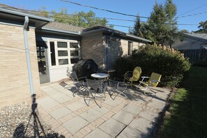 Eine Terrasse mit Tisch, Stühlen, einem überdachten Grill und einer Ziegelwand.