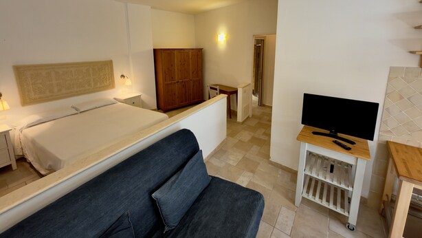 Una habitación de hotel con cama, sofá, televisión sobre un mueble bajo, armario y una mesita.