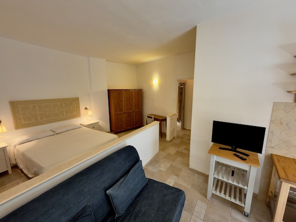 A hotel room with a bed, a sofa, a TV on a stand, a wardrobe, and a small table. - Residence Abbaechelu Santa Margherita Pula (Pula)