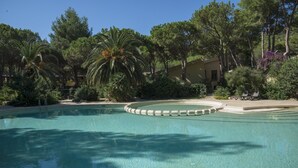 Una piscina con un deck circular, rodeada de árboles y un edificio.