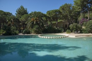 A swimming pool with a circular deck, surrounded by trees and a building. - Residence Abbaechelu Santa Margherita Pula (Pula)