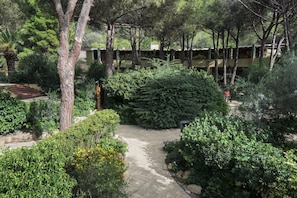 A garden pathway surrounded by dense foliage and trees, leading to a building with a wooden fence. - Residence Abbaechelu Santa Margherita Pula (Pula)