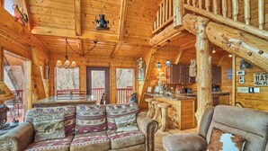 Un intérieur de chalet chaleureux, avec un revêtement mural en bois, un canapé agrémenté de coussins à motifs, un coin repas et un bar.