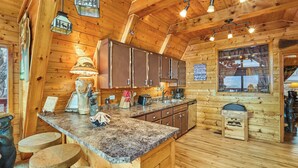 L’intérieur d’un chalet en bois comprend un coin cuisine, des tabourets en bois et une fenêtre donnant sur un paysage agréable.