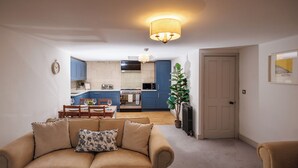 A living room with a sofa, a dining table with chairs, a kitchen area with blue cabinets, and a door. - Georgian Gem Penthouse in Bath Centre! (Bath)