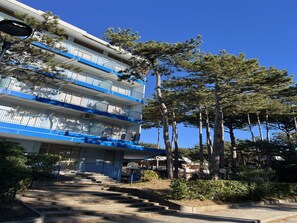 A multi-story building with balconies, a staircase leading to the entrance, and surrounding trees. - Cozy Accommodation Just 250mt From the Beach (Lignano Sabbiadoro)