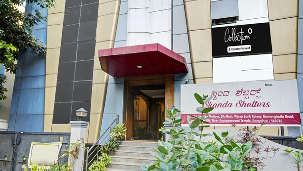 A building entrance with a red awning, a sign for 'Shanda Shelters', and a staircase leading to the entrance. - Deluxe Skanda Shelters (Bengaluru)