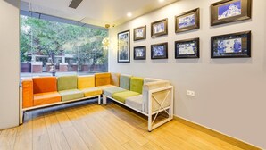 Un área de espera moderna con un sofá colorido, cuadros enmarcados en la pared y un amplio ventanal con vistas a la vegetación.