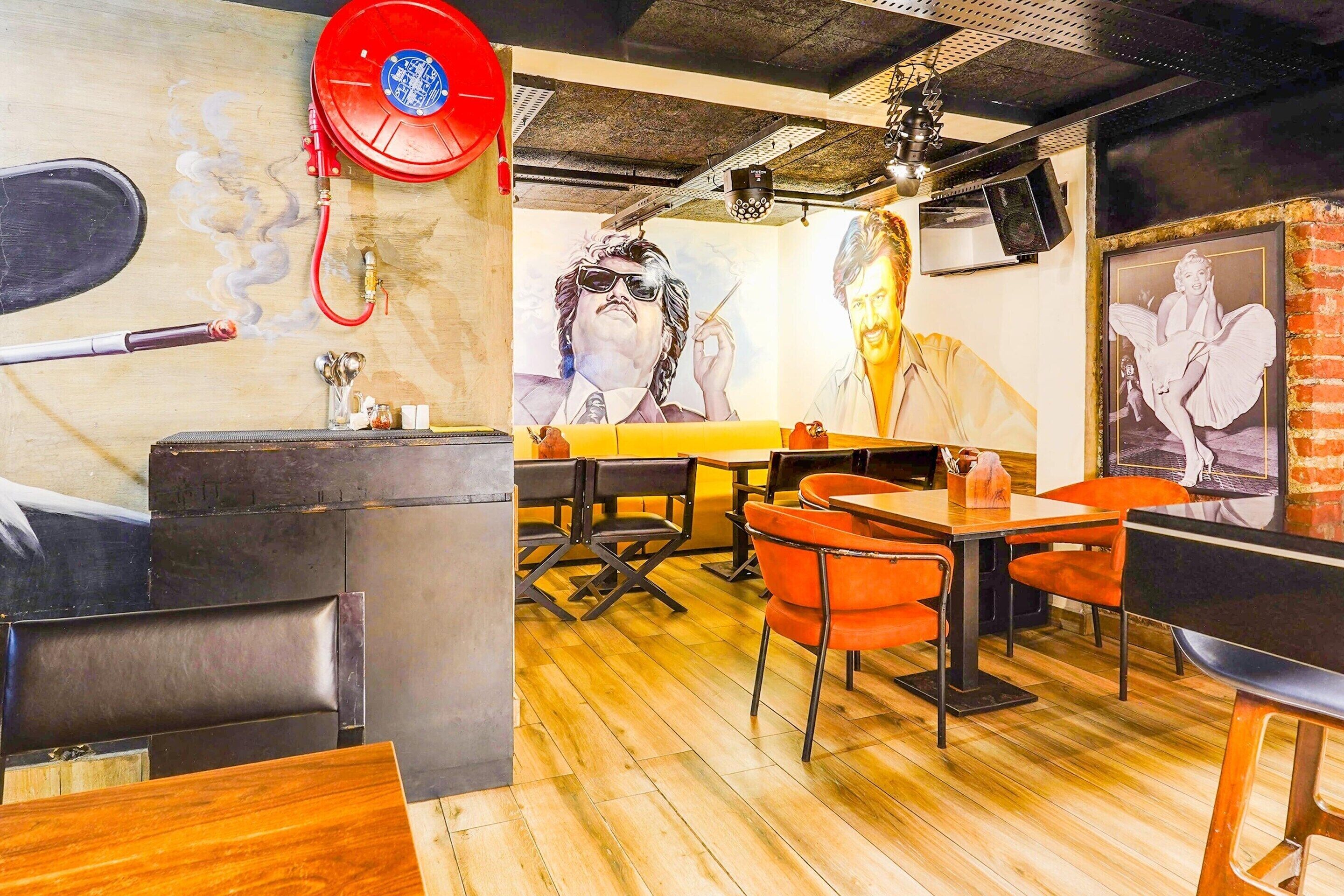 L’intérieur d’un restaurant présente un plancher en bois, des chaises orange et une fresque murale.