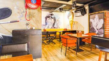 L’intérieur d’un restaurant présente un plancher en bois, des chaises orange et une fresque murale.