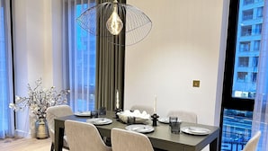 Une salle à manger moderne avec une grande table, des chaises, un luminaire suspendu et une vue sur un bâtiment par la fenêtre.