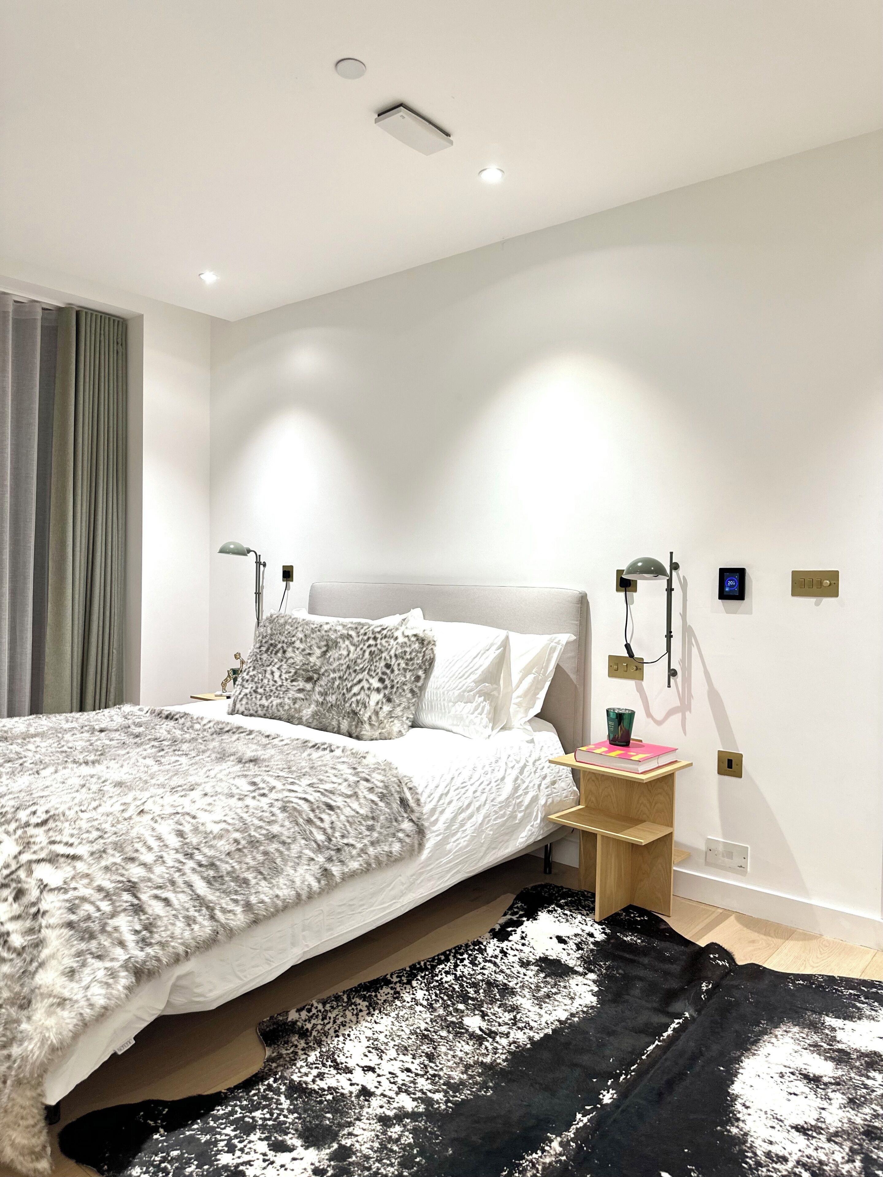 A modern bedroom with a bed, bedside tables, a lamp, and a digital thermostat.