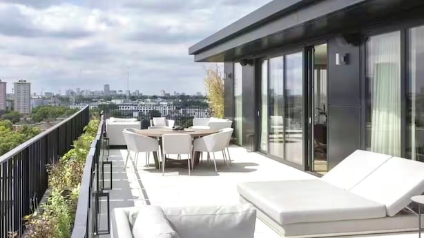 Une terrasse sur le toit, avec une table et des chaises pour les repas, un canapé et une balustrade en verre donnant sur le paysage urbain.