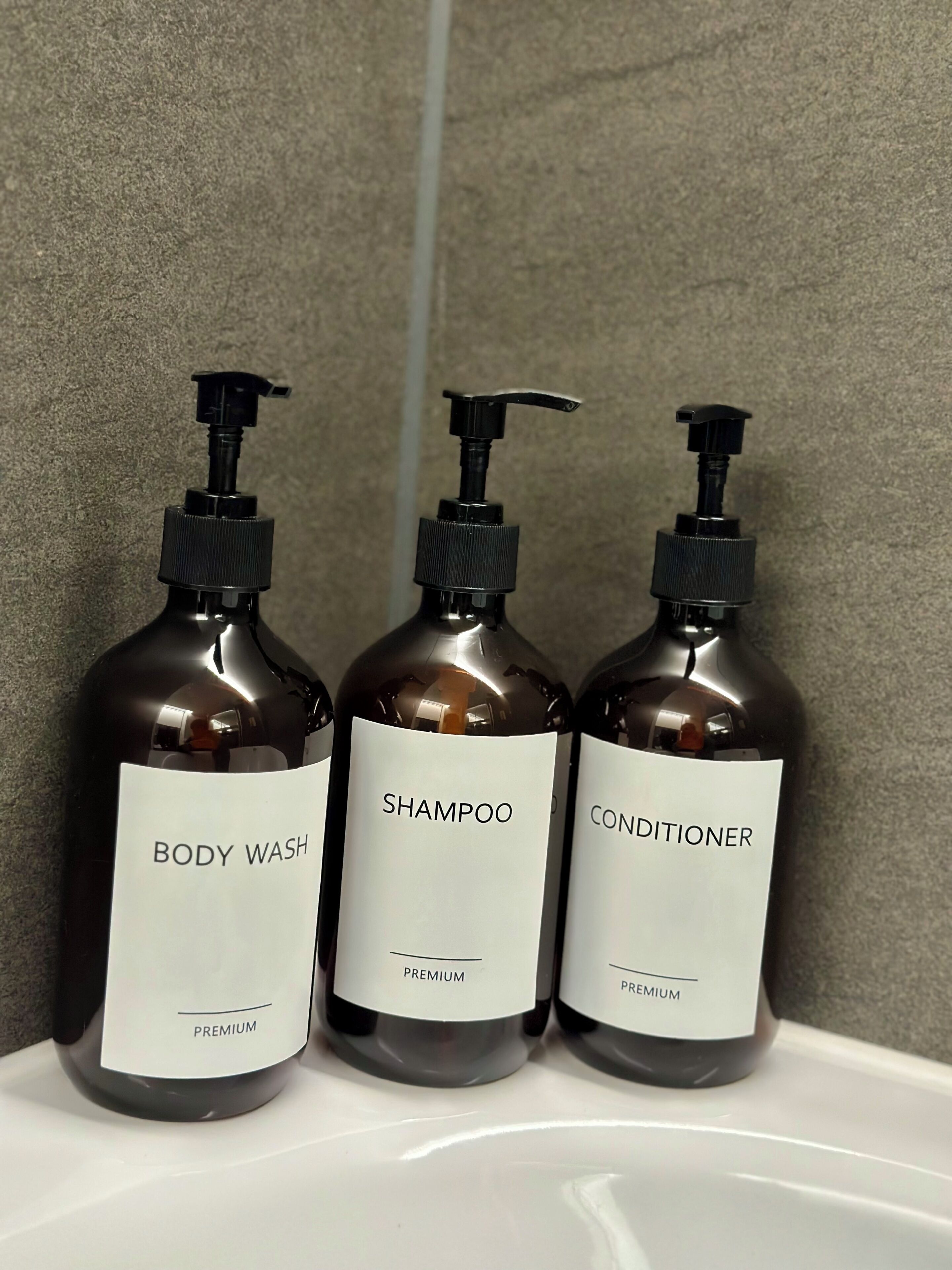 Trois bouteilles de gel douche, de shampoing et d’après-shampoing sur une surface blanche.