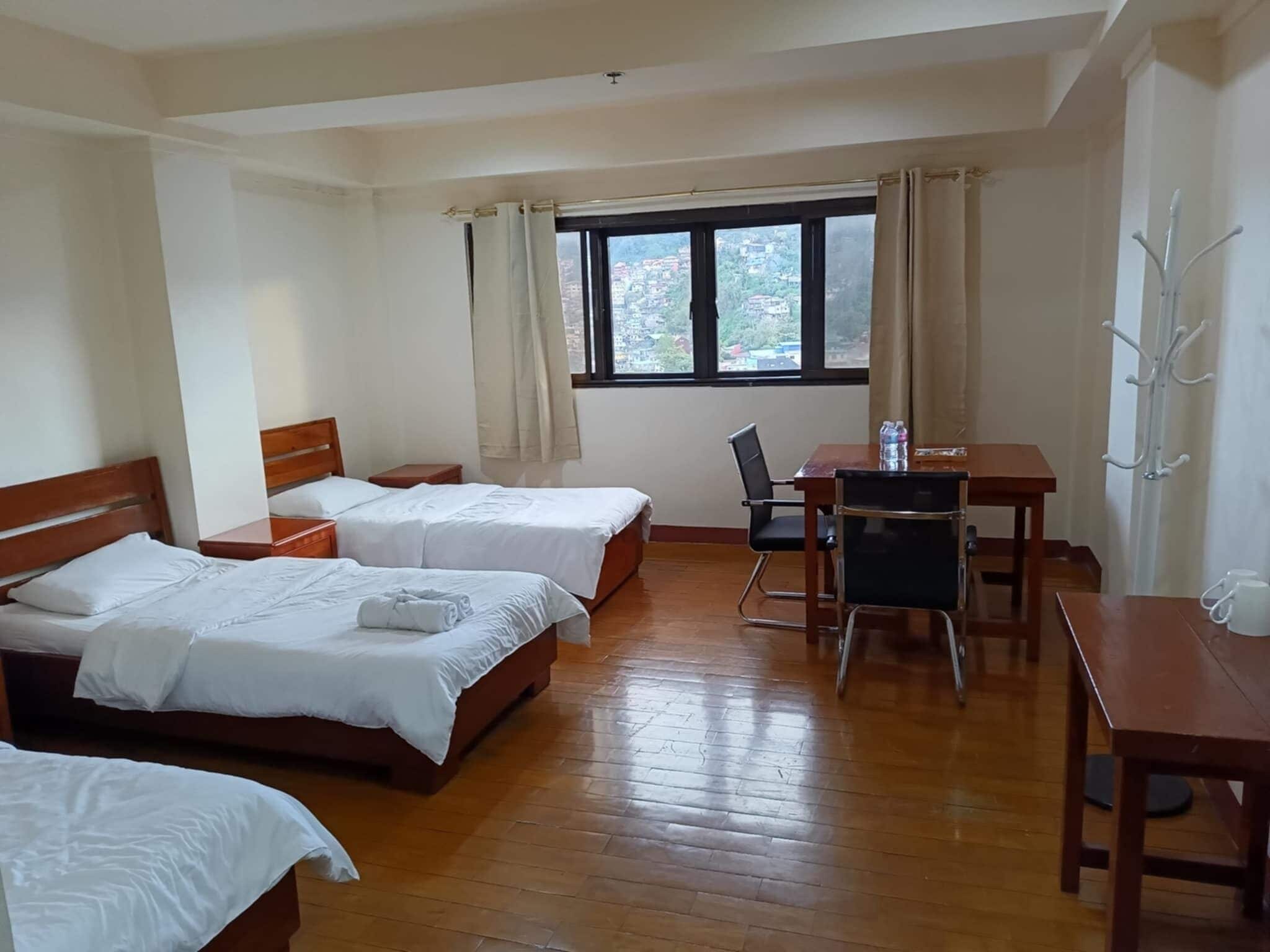 Une chambre d’hôtel avec deux lits, un bureau, une chaise et une vue sur le paysage urbain par la fenêtre.