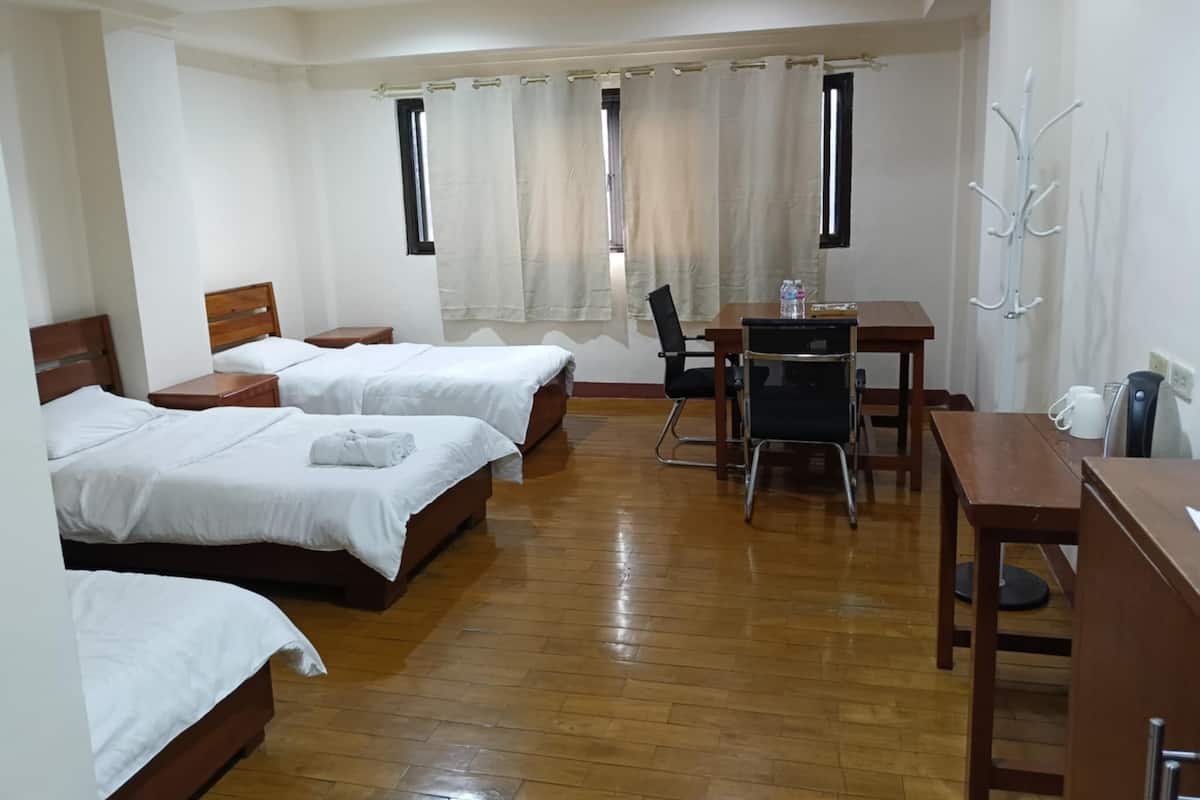 Habitación de hotel con dos camas, un escritorio, una silla, perchero y ventana con cortinas.